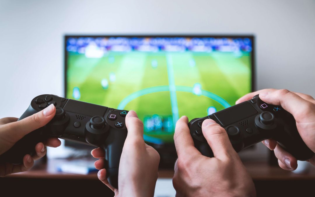 Two people hold black game controllers while playing a soccer video game displayed on a television screen in the background.