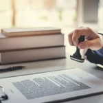 Certified Translation and Document Authentication Services | PSP Languages – PSP Languages Certified translation document being stamped on a desk with legal books and paperwork in the background.