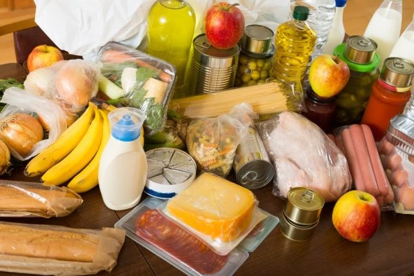 Assorted consumer goods including fresh fruits, vegetables, dairy products, packaged foods, canned items, meat, and household essentials displayed on a table.