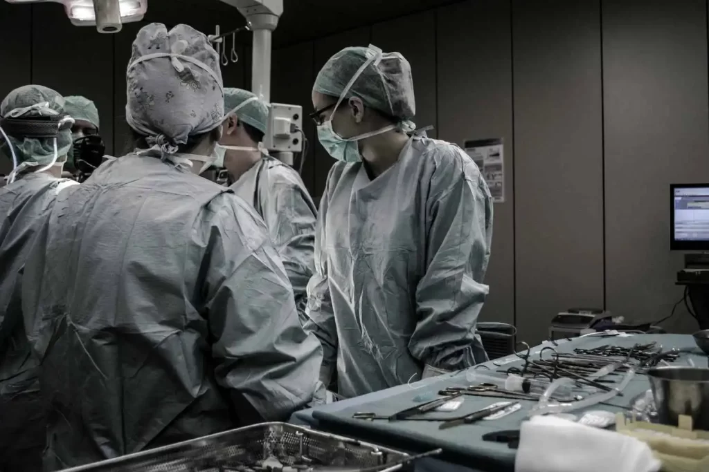 Surgical team in scrubs and masks gathered around operating table, tools laid out on a tray in a medical theater