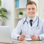 Professional doctor in white coat working at desk with laptop and medical documents