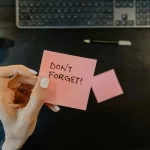Hand holding a reminder note at a workspace, representing timely professional translation and localization project management.