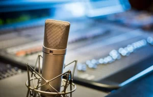Professional condenser microphone in a recording studio with an audio mixing console in the background, representing voiceover, dubbing, and audio localization services.Show more lines